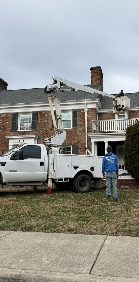 Bucket truck with the boom raised to the roofline of a brick house.