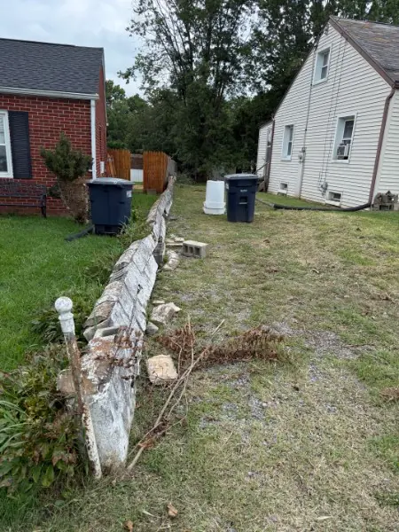 Collapsed concrete retaining wall and debris between a brick house and a white house, before demolition.